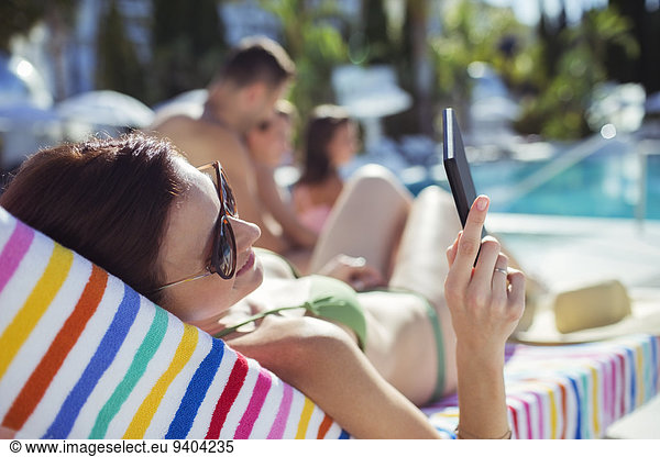 Woman sunbathing and texting by swimming pool