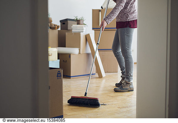 Woman sweeping the floor surrounded by cardboard boxes in an empty room