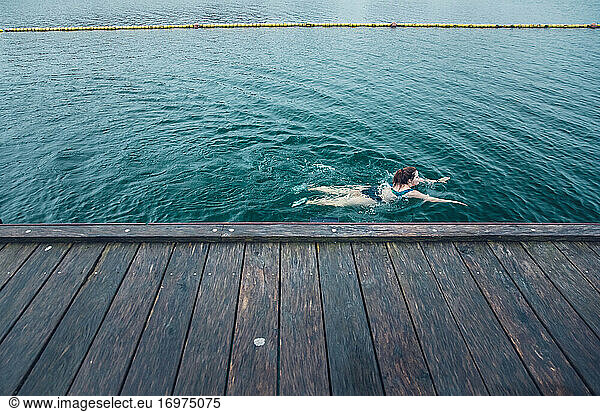 Woman Swimming Solo Next to Wooden Dock in Cold Water in CDenmark