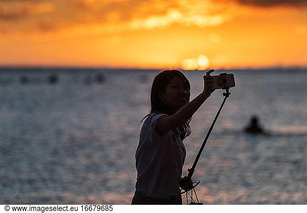 Woman takes selfie in front of ocean at sunset