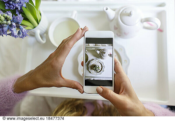 Woman taking photo of cupcake through smart phone in bed at home
