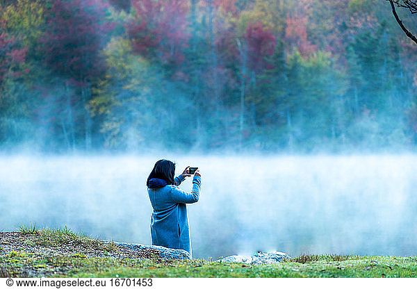 Woman taking photo with phone of the fog and New England fall foliage.