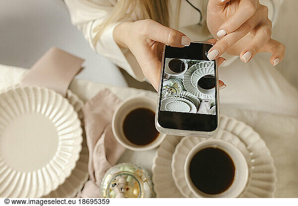 Woman taking picture of coffee through smart phone at home