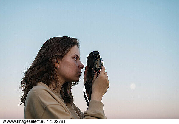 Woman taking pictures outdoor with a film camera during a sunset