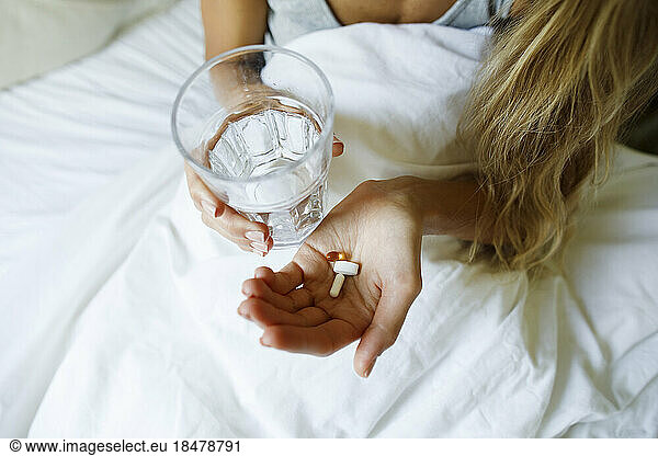Woman taking pills with glass of water in bed at home