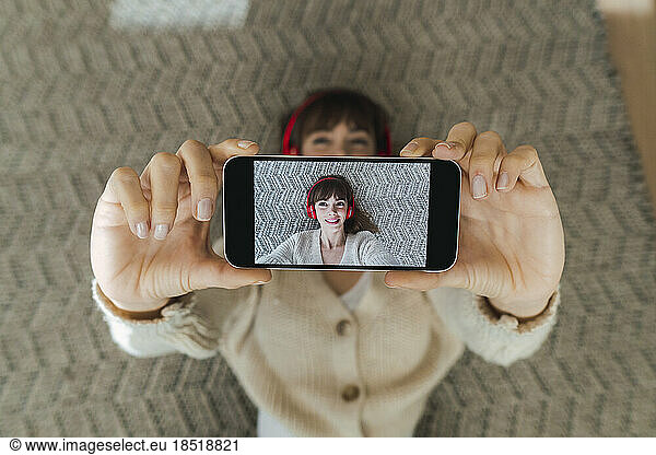 Woman taking selfie through smart phone lying on floor at home