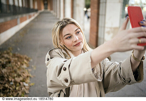 Woman taking selfie through smart phone on footpath