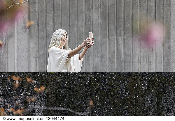 Woman taking selfie while standing by retaining wall