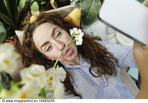 Woman taking selfie with flower on puckering lips