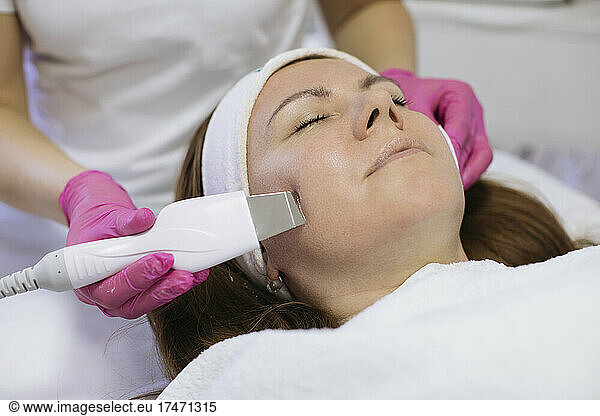 Woman taking ultrasonic facial treatment in salon