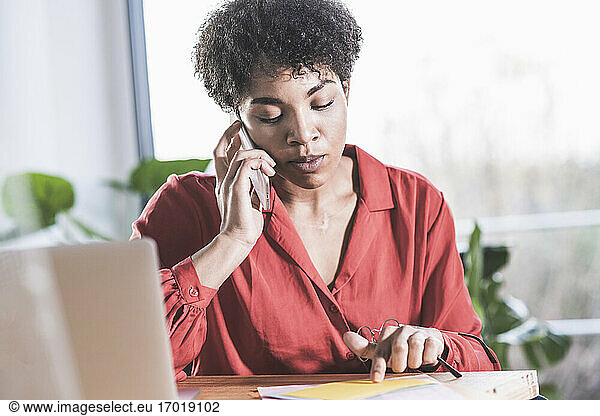 Woman talking on mobile phone and looking at documents at desk