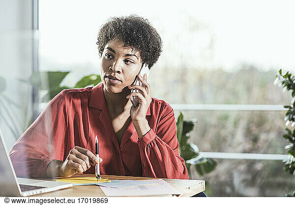 Woman talking on mobile phone and looking at laptop at desk