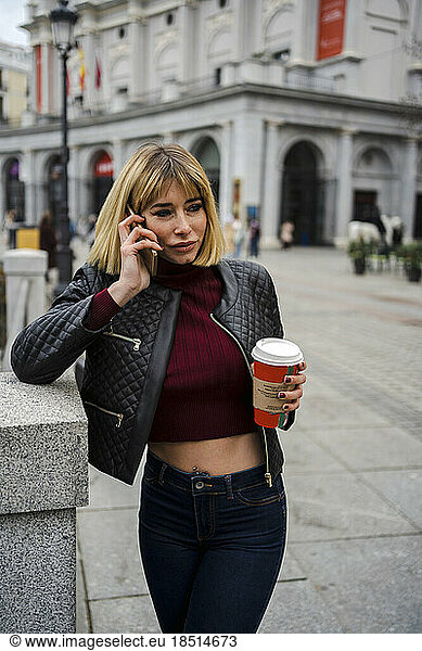 Woman talking on smart phone holding disposable coffee cup