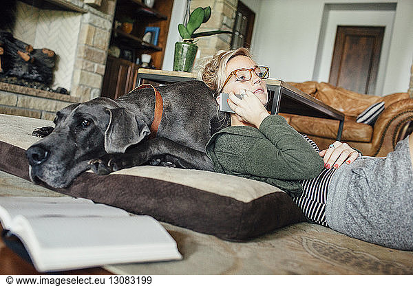 Woman talking on smart phone while lying on Great Dane at home