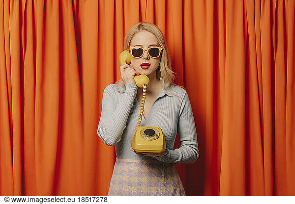 Woman talking on vintage landline phone in front of orange curtains
