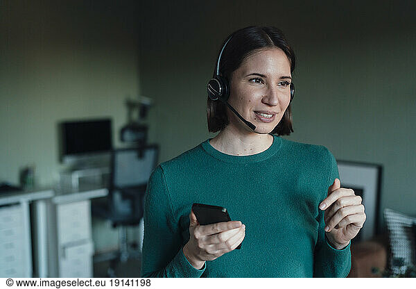 Woman talking through headset holding smart phone at home