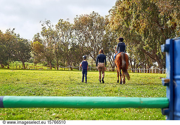 Woman teaching girls horseback riding in sunny rural grass paddock