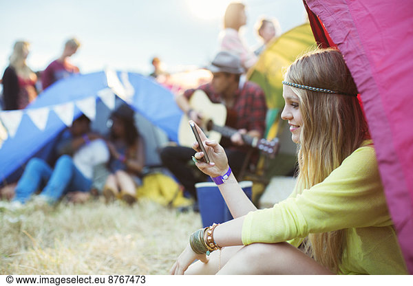 Woman text messaging with cell phone at tent at music festival