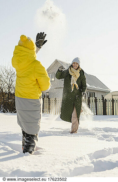 Woman throwing snowball at son standing on deep snow in winter