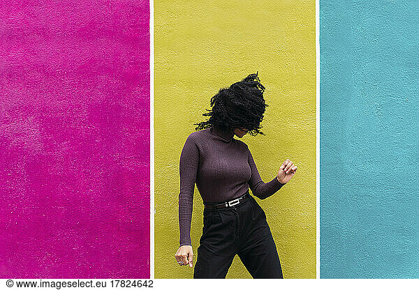 Woman tossing hair standing in front of multi colored wall
