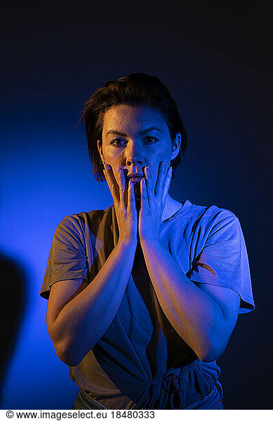 Woman touching face with blue neon lighting against colored background
