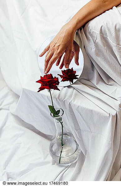 Woman touching red rose in vase with reflection on mirror