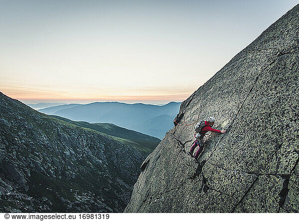 Woman traversing rock climb in White Mountains of NH at sunrise