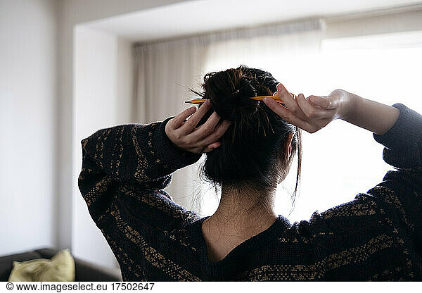Woman tying hair with pencil at home