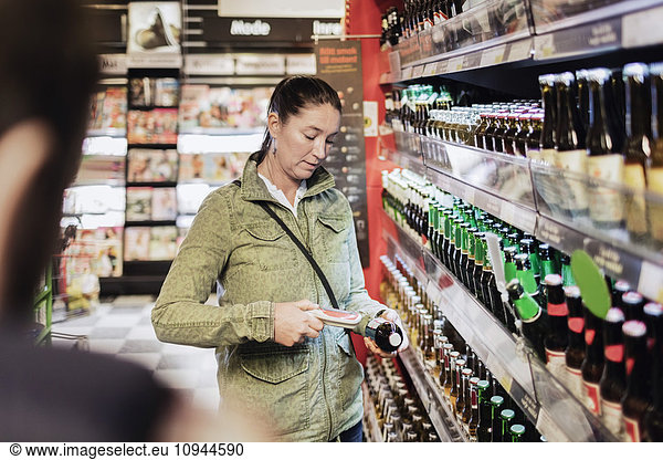 Woman using bar code reader on beer bottle at supermarket