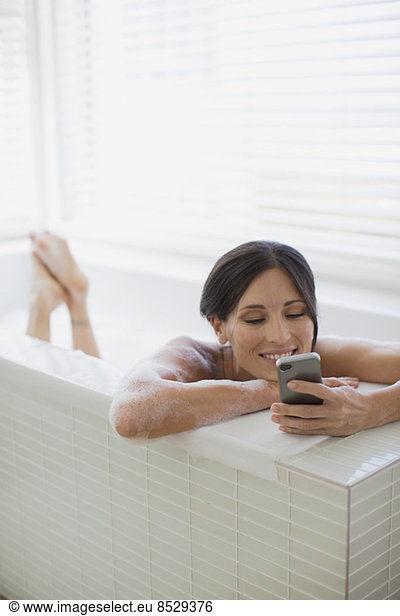 Woman using cell phone in bathtub