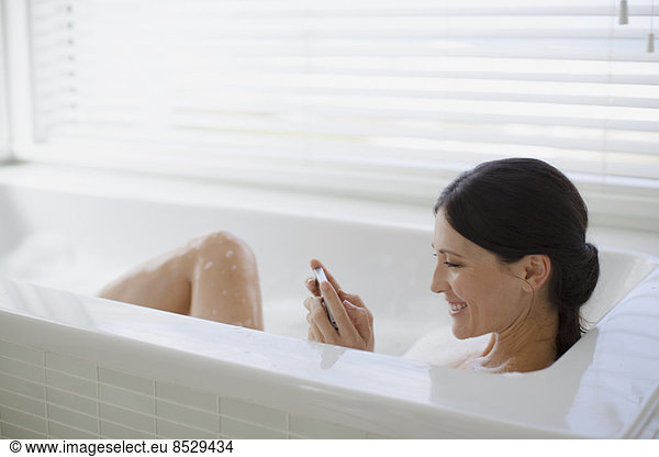 Woman using cell phone in bubble bath