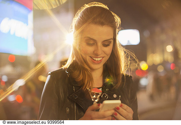 Woman using cell phone on city street at night