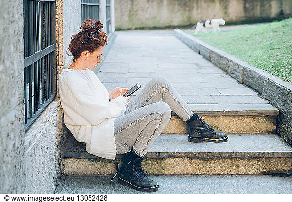 Woman using cellphone on step by building