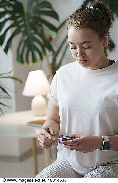 Woman using digital glucometer sitting at home