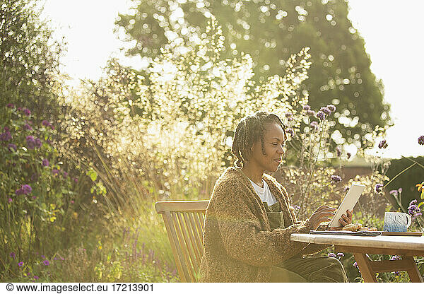 Woman using digital tablet at sunny idyllic garden patio table