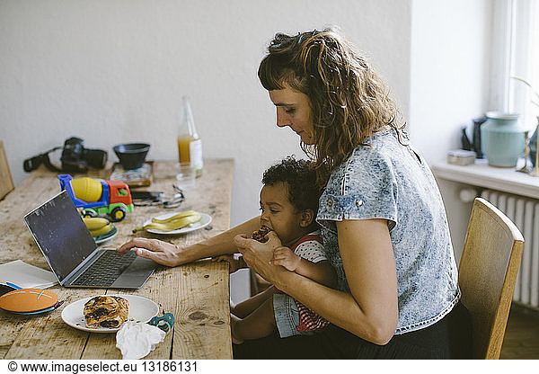 Woman using feeding food to daughter while sitting at dining table in house