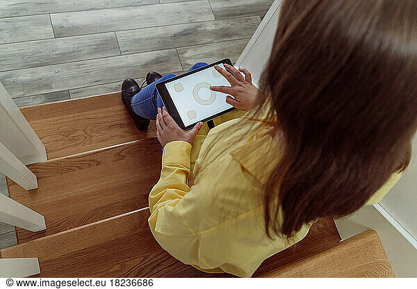 Woman using home automation app through tablet PC sitting on steps
