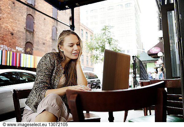 Woman using laptop computer sitting at sidewalk cafe