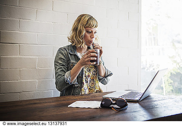 Woman using laptop computer while drinking ice tea in cafe