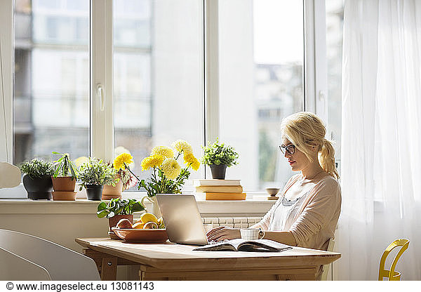 Woman using laptop computer while sitting by window at home