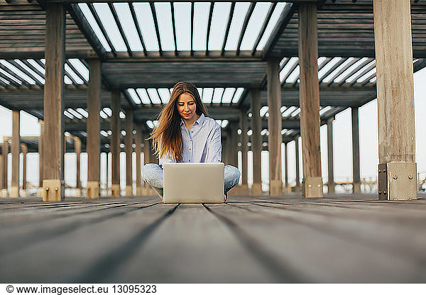 Woman using laptop computer while sitting on pier