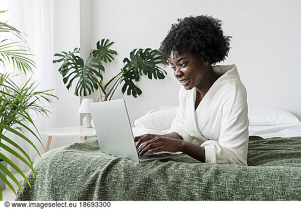 Woman using laptop lying on bed at home