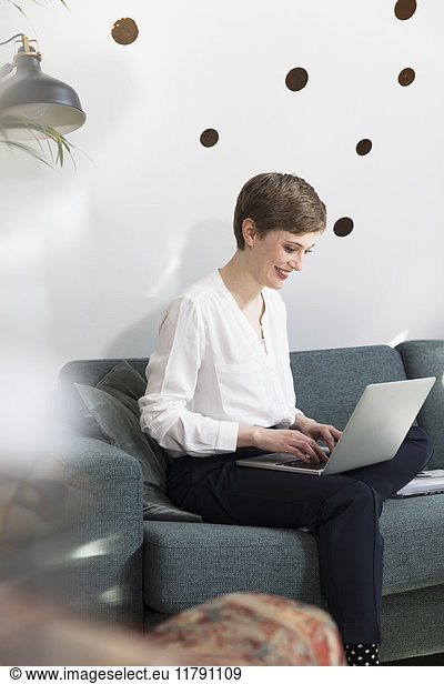 Woman using laptop on couch in modern office