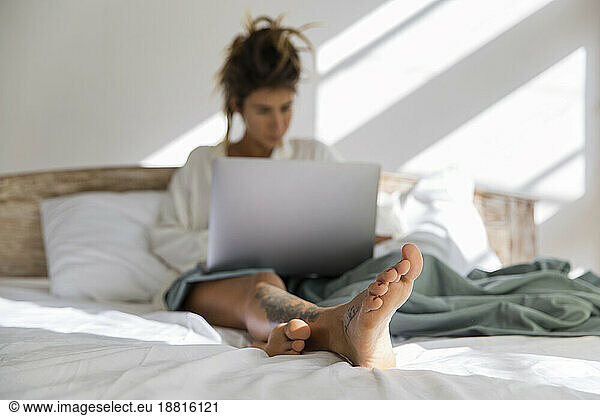Woman using laptop sitting on bed at home