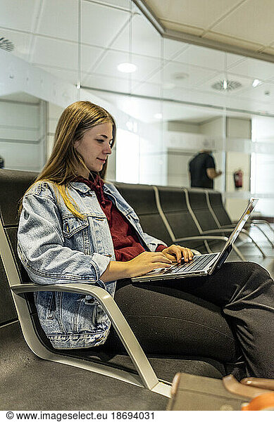 Woman using laptop sitting on seat at airport