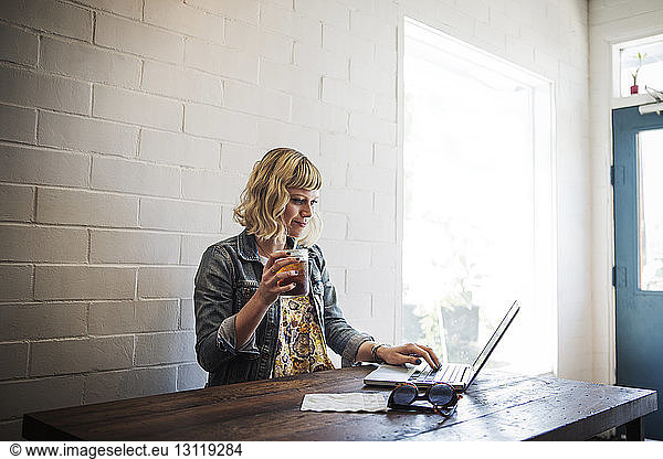 Woman using laptop while holding iced tea glass in cafe