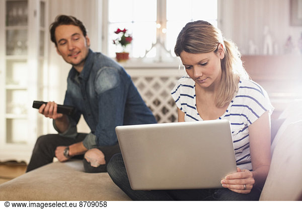 Woman using laptop while man looking at her in house