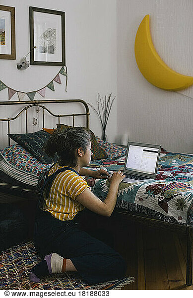 Woman using laptop while sitting near bed at home