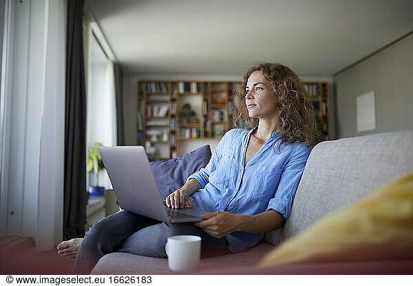 Woman using laptop while sitting on sofa at home