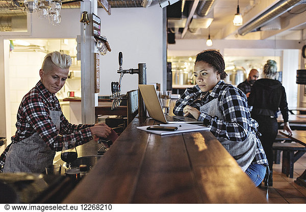 Woman using laptop while standing by partner at bar counter